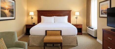 A hotel room with a large bed, two bedside tables, a television, a chair, and a bench.