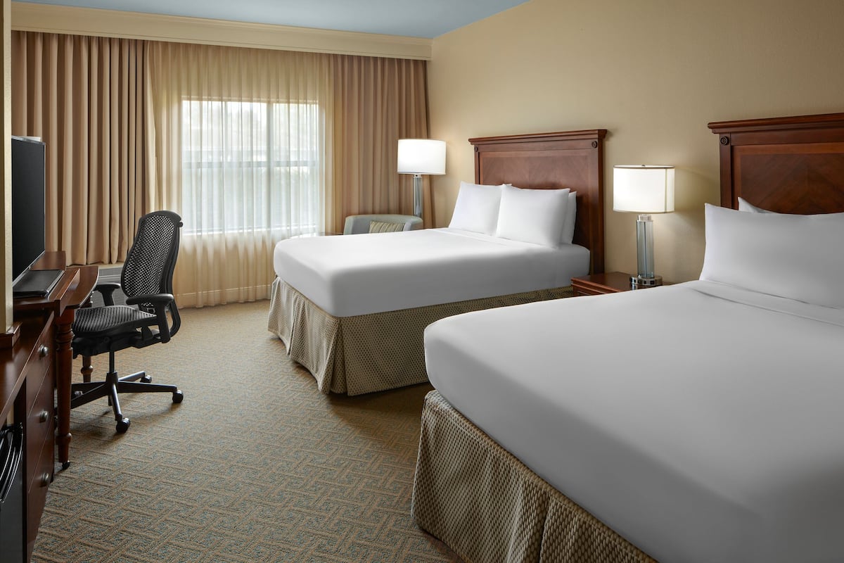 A hotel room with two beds, a desk with a computer, a chair, and a lamp.