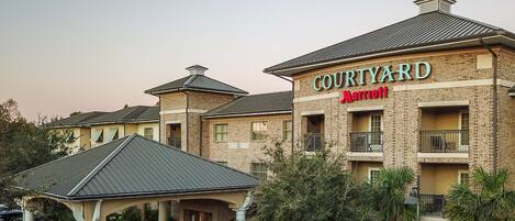 Um hotel Courtyard Marriott com fachada de tijolos, várias varandas e uma área de entrada coberta.