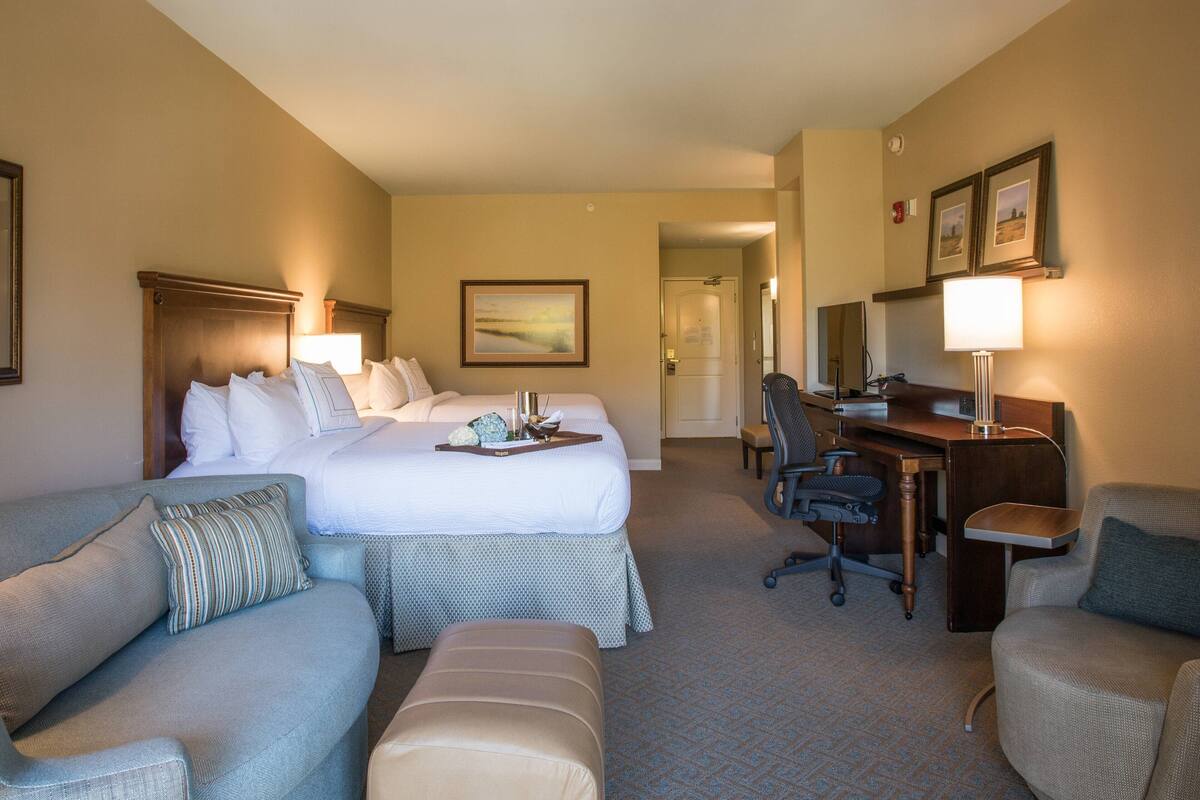 A hotel room with a large bed, two bedside tables, a desk, a chair, a sofa, and a small table.