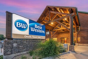 A Best Western sign in front of a wooden building with a stone base and a covered entrance. - Best Western Devils Tower Inn (Hulett)