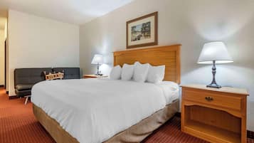 A hotel room with a large bed, two bedside tables with lamps, a wooden headboard, a framed picture on the wall, and a red carpeted floor.
