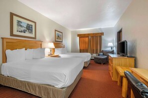 A hotel room with two beds, a desk with a television, a chair, and a small sofa.