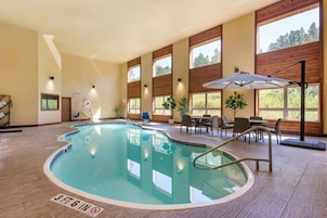 Una piscina interior con indicador de profundidad de 1 metro 17 centímetros, rodeada de paredes de madera, ventanas amplias y un área de descanso con mesas y sillas.
