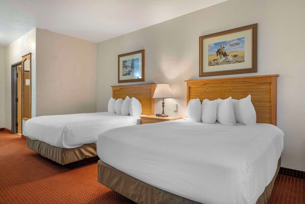 A hotel room with two single beds, a wooden headboard, a nightstand with a lamp, and two framed pictures on the wall.