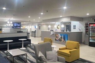 A modern hotel lobby with seating areas, a reception desk, and a Coca-Cola refrigerator.