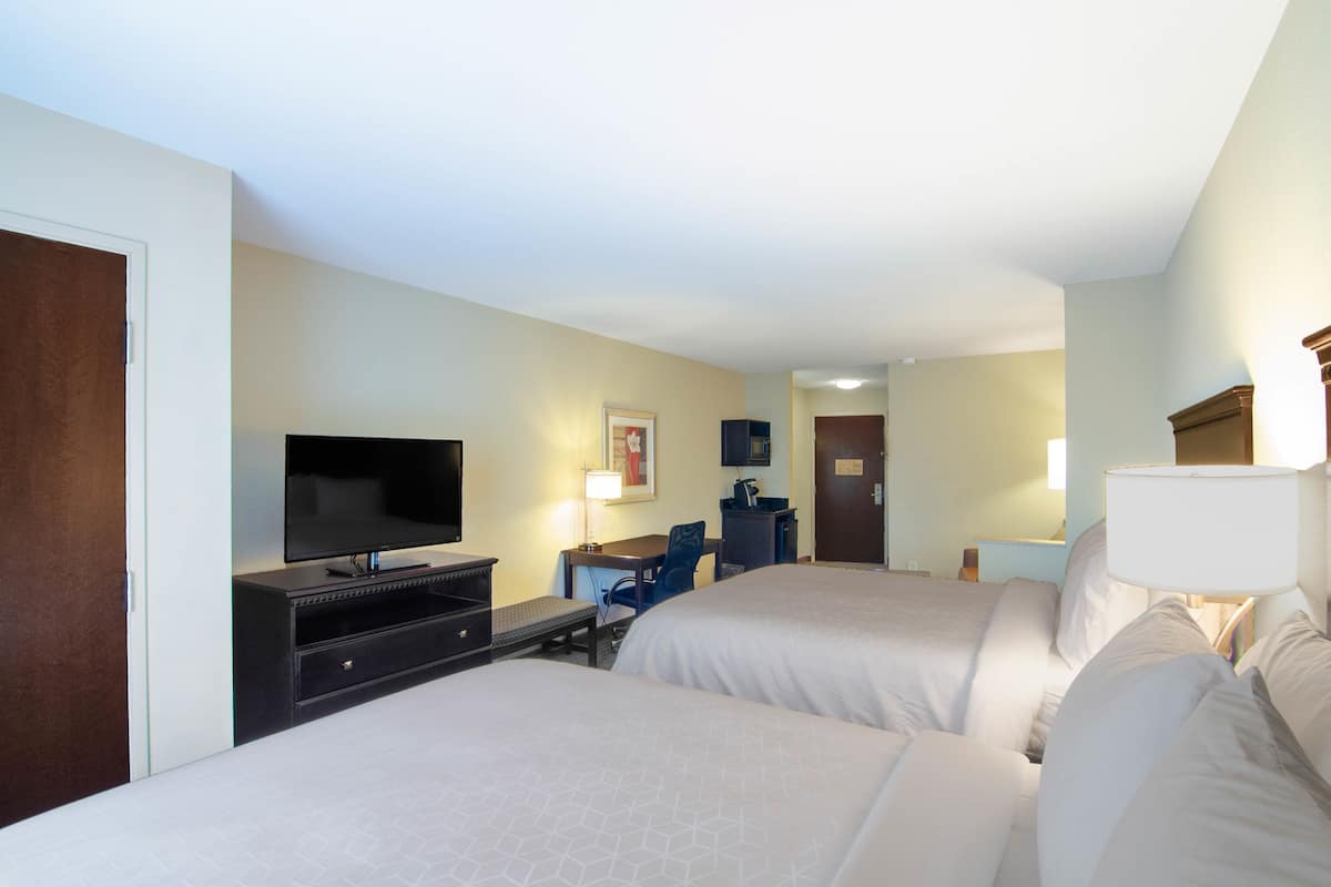 A hotel room with two beds, a TV, a desk, and a chair.