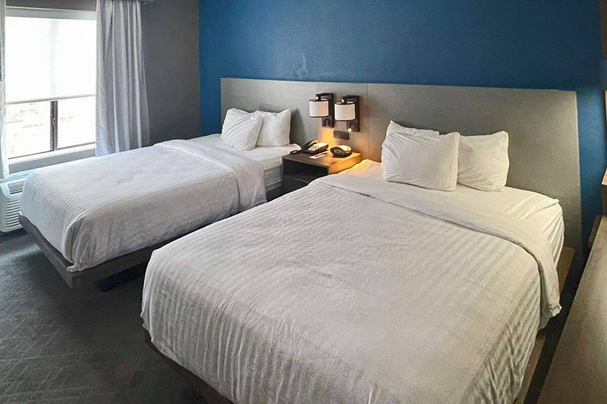A hotel room with two beds, a nightstand with a lamp, and a window with curtains.