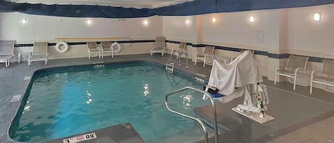 Una piscina interior con agua cristalina, un trampolín y sillones de descanso alrededor del borde.