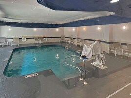 An indoor swimming pool with clear water, a diving board, and lounge chairs around the perimeter.
