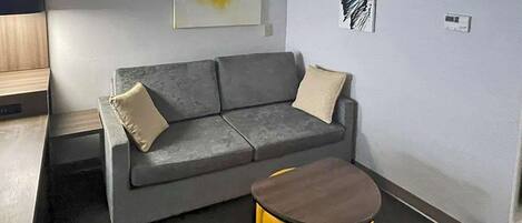 A modern living room with a grey sofa, two beige cushions, and a small yellow stool.
