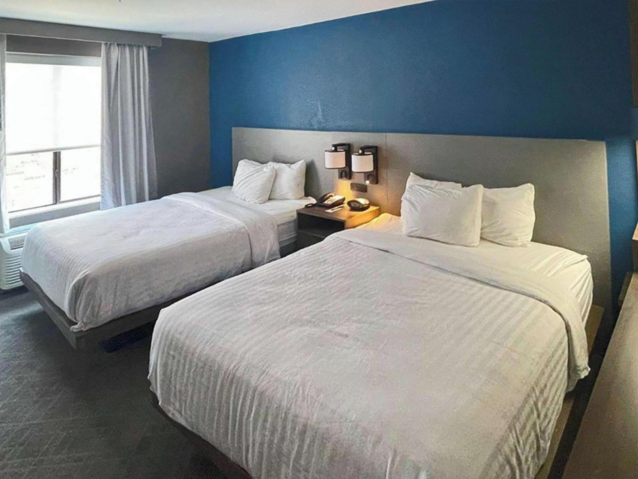 A hotel room with two beds, a nightstand with a lamp, and a window with curtains.