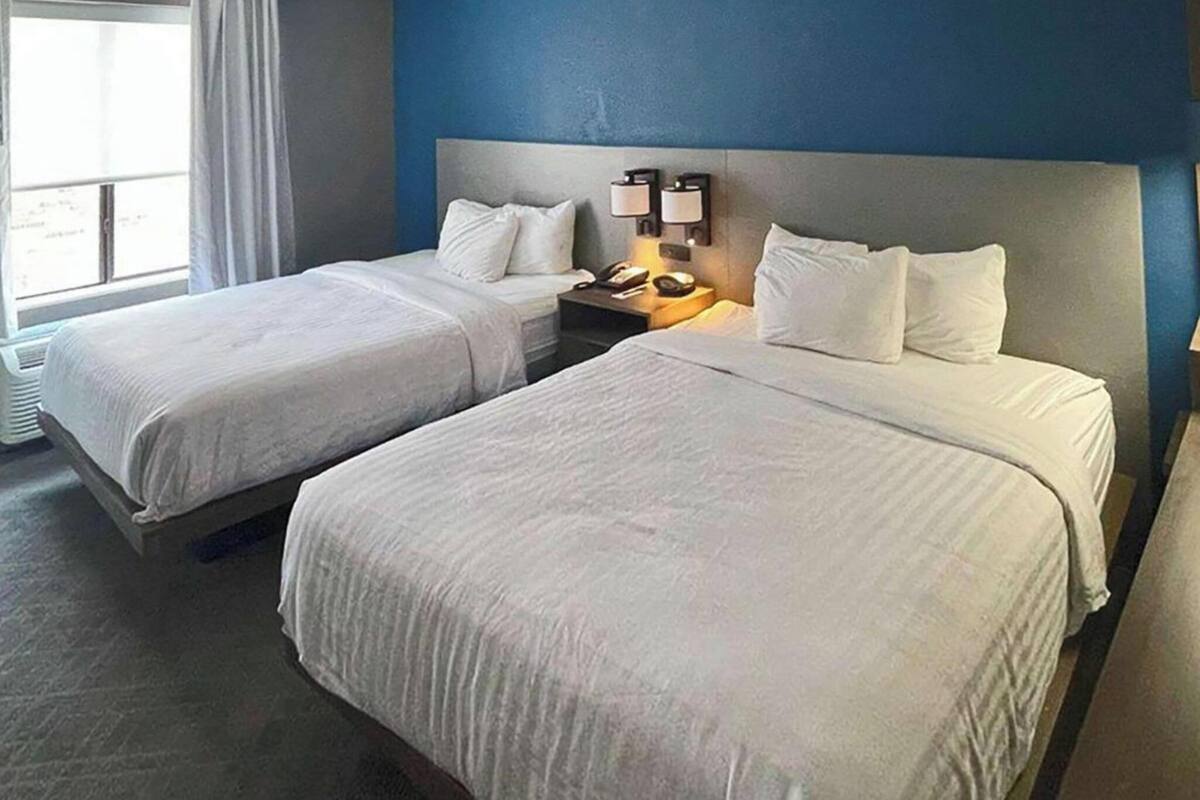 A hotel room with two beds, a nightstand with a lamp, and a window with curtains.