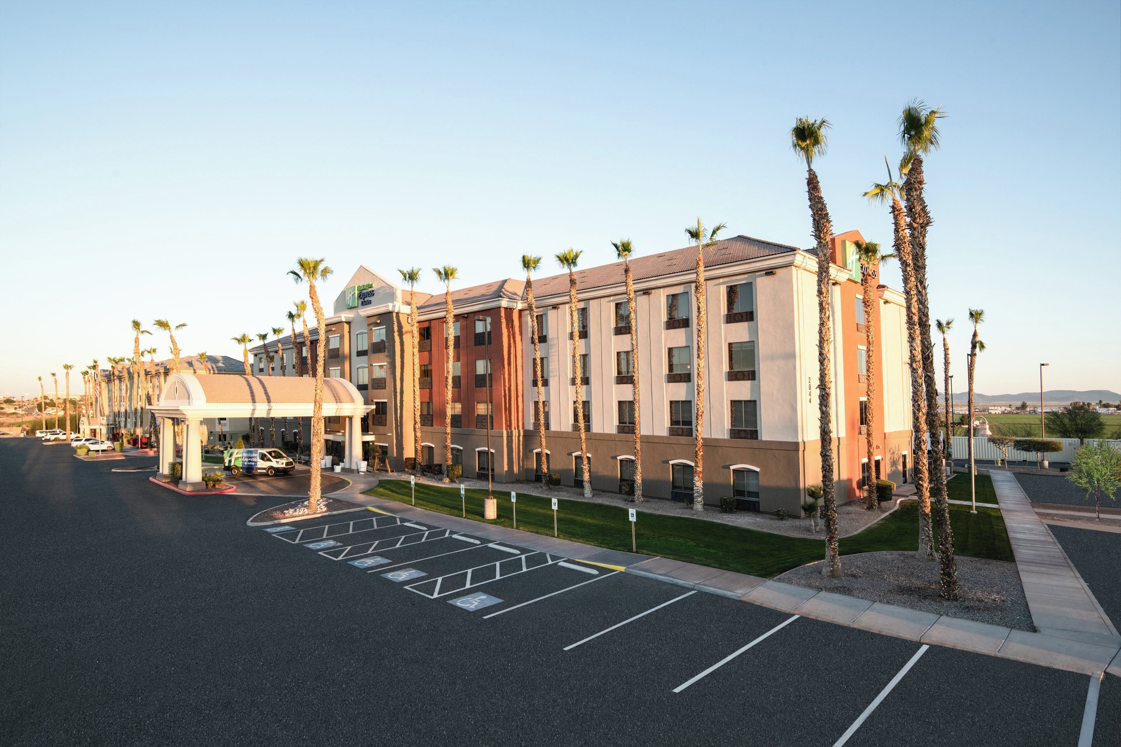 A hotel with a parking lot, a covered entrance, and palm trees.