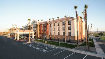 A hotel with a parking lot, a covered entrance, and palm trees.