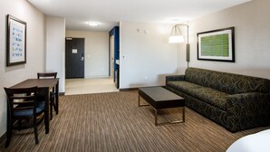 Habitació d'hotel amb taula de menjador, cadires, sofà, taula auxiliar i làmpada.