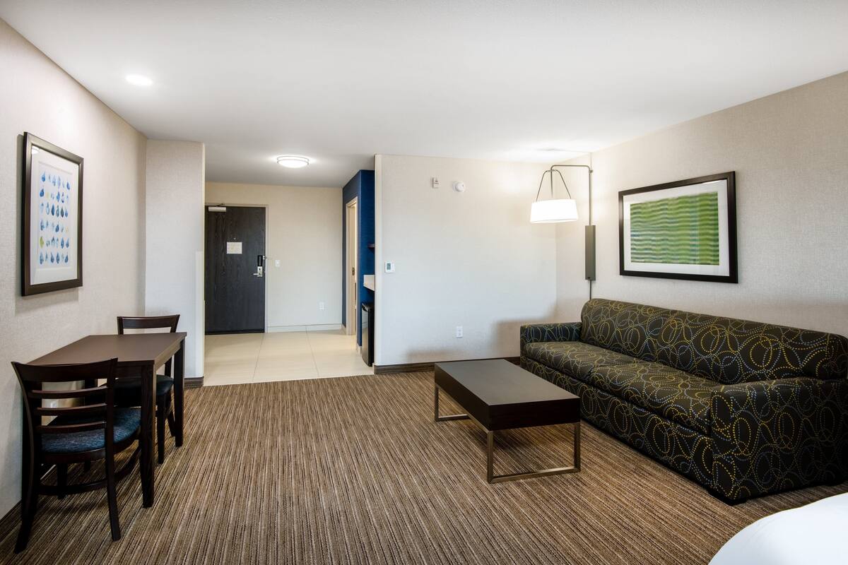 A hotel room with a dining table, chairs, a sofa, a coffee table, and a lamp.