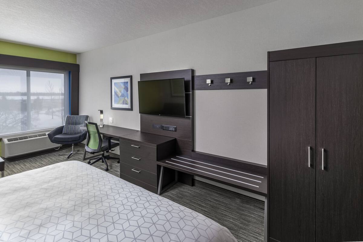 A hotel room with a large bed, a desk with a chair, a TV mounted on the wall, and a wardrobe.