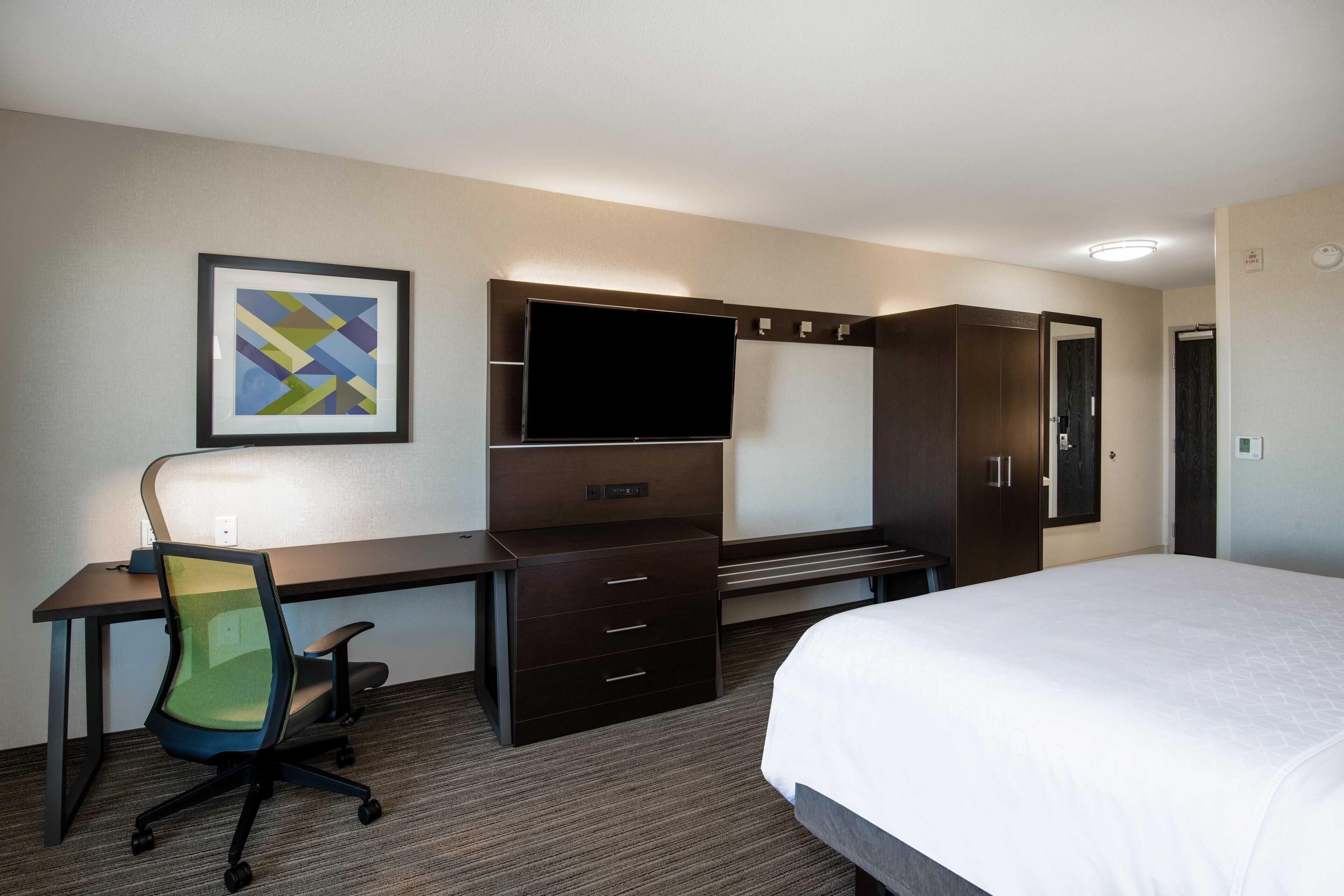 A hotel room with a bed, a desk with a chair, a television, and a wardrobe.