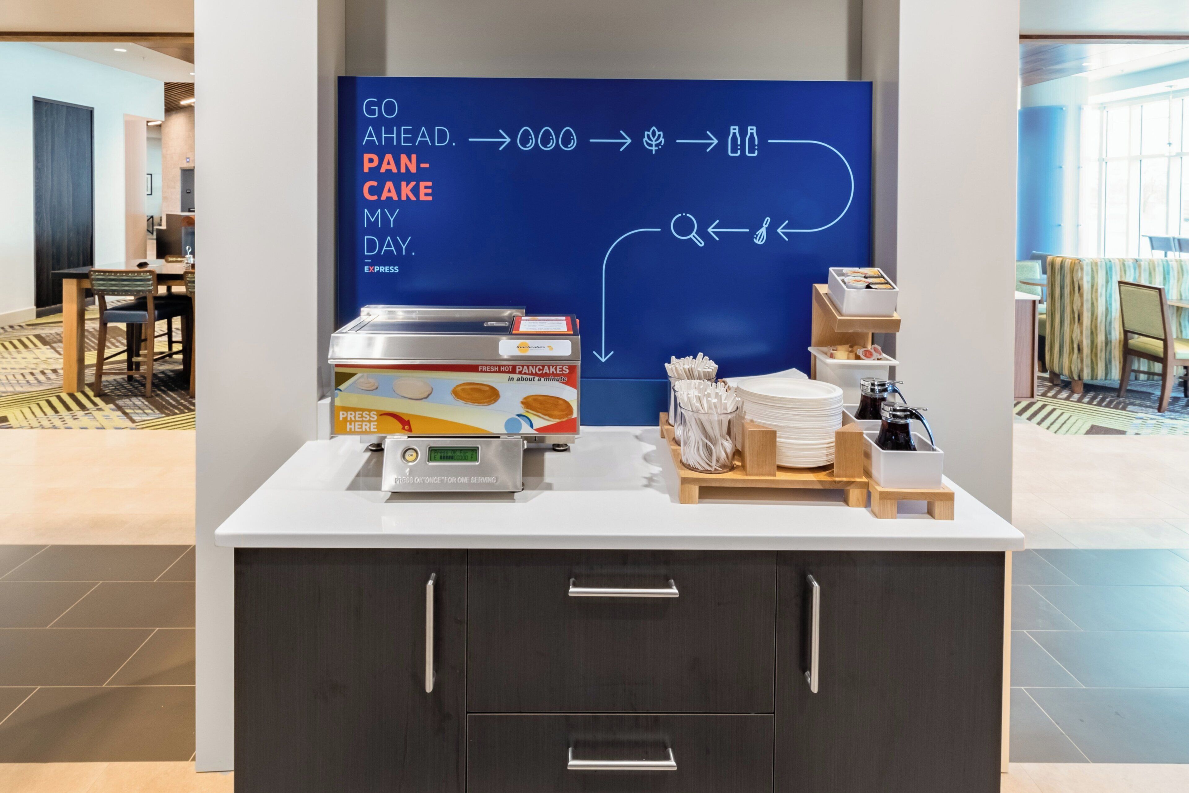 A breakfast station with a sign indicating the process of making pancakes, a fresh hot pancake dispenser, and a selection of condiments and utensils.