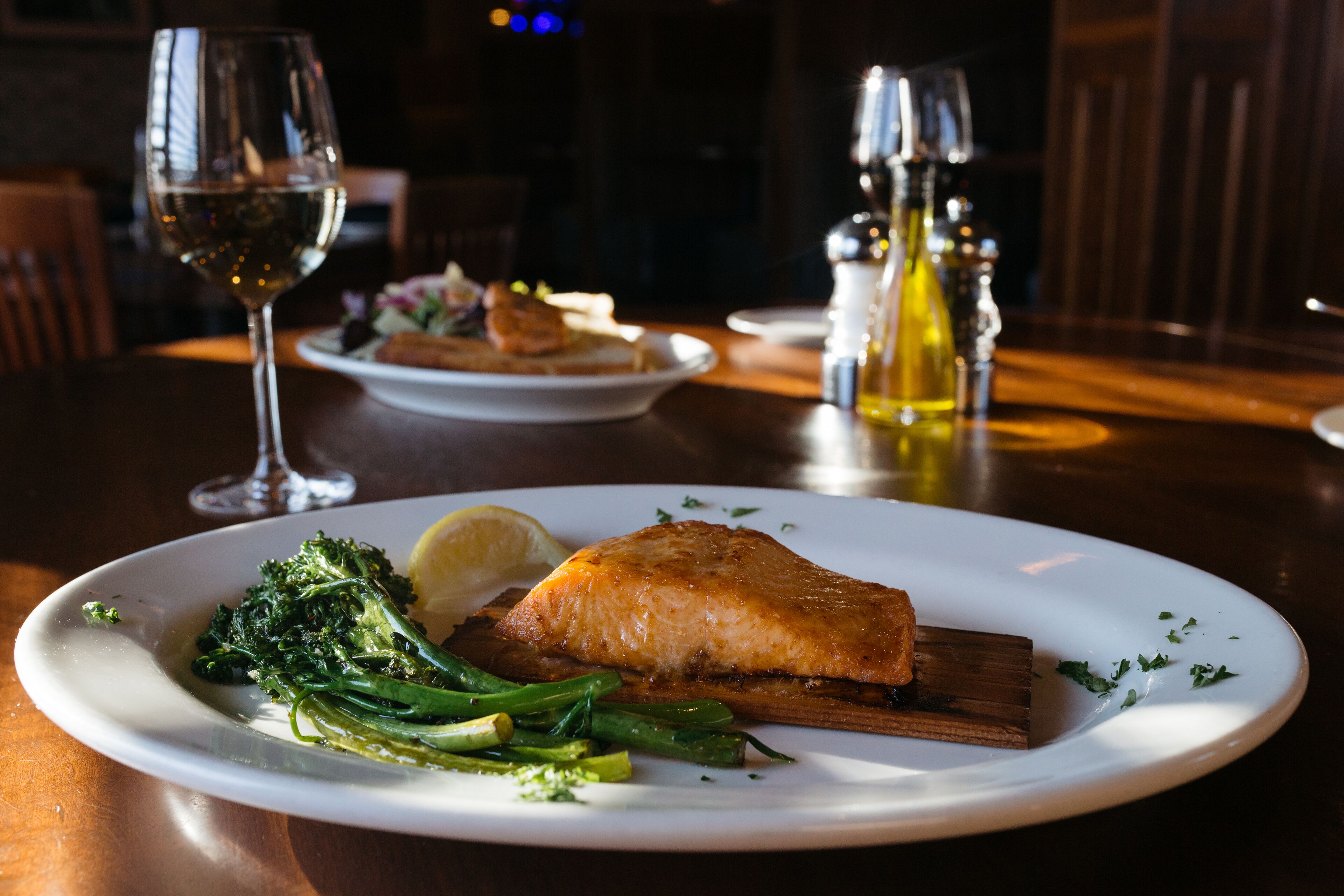 A plate of food with salmon, broccoli, and lemon on a wooden table.