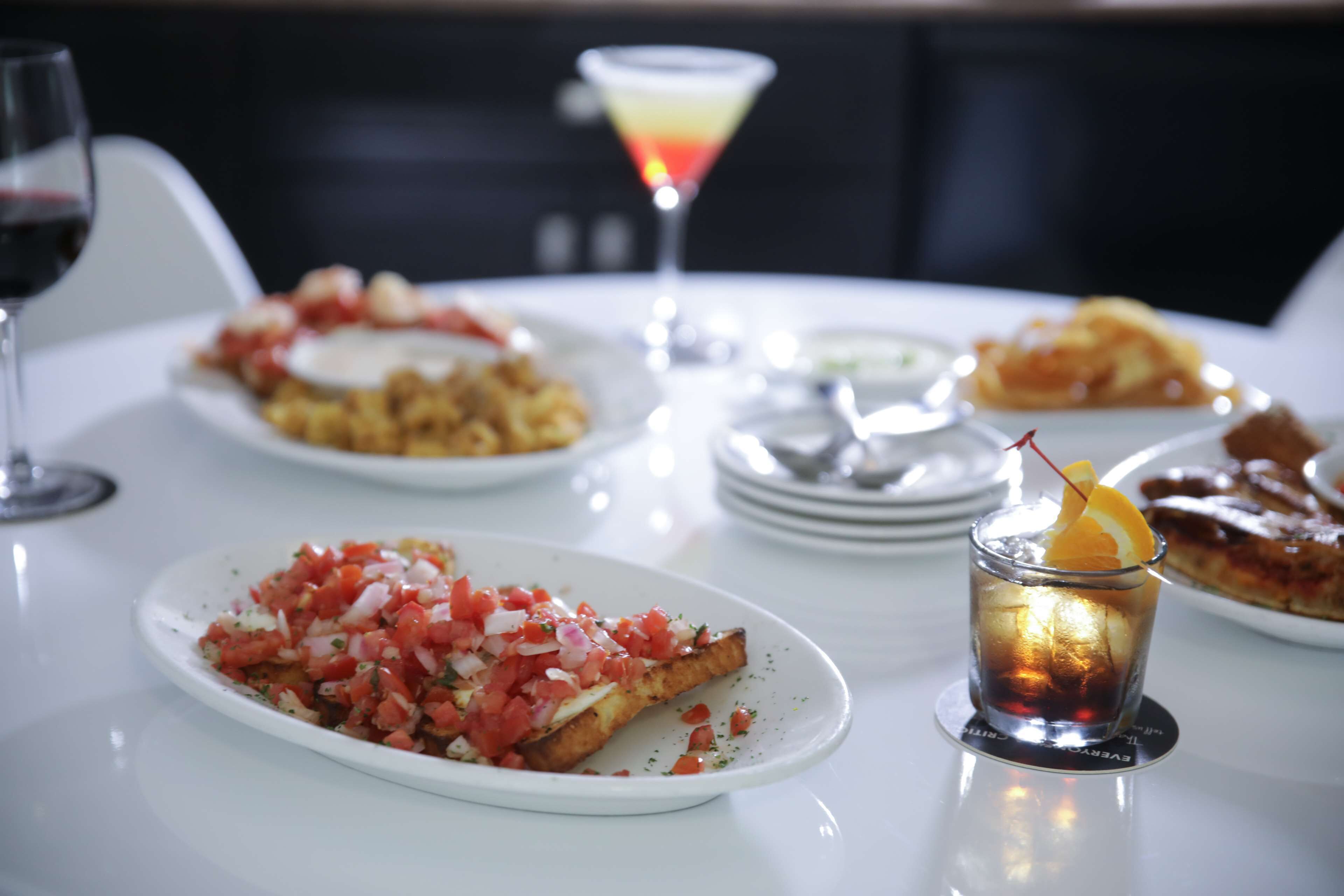 A dining table with various dishes, a martini glass, and a drink with an orange garnish.