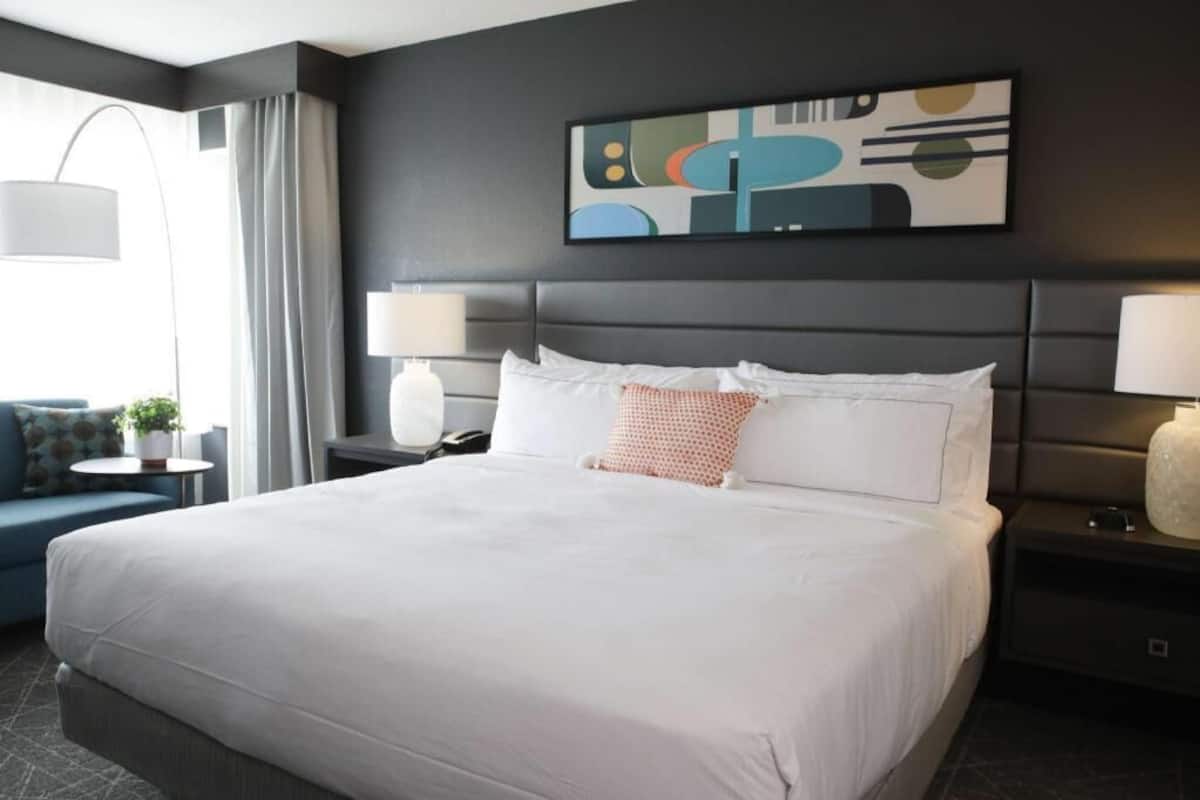 A hotel room with a large bed, two bedside tables with lamps, a sofa, and a wall-mounted abstract painting.