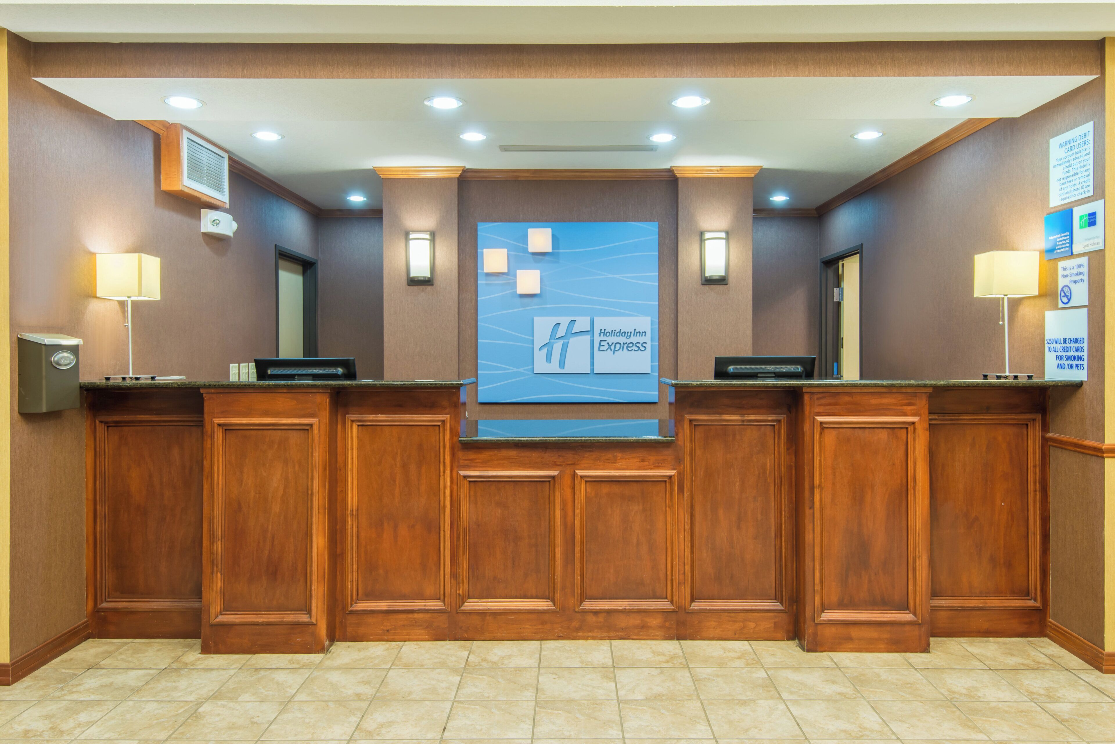 A reception desk with a Holiday Inn Express sign, a digital display, and a non-smoking property notice.