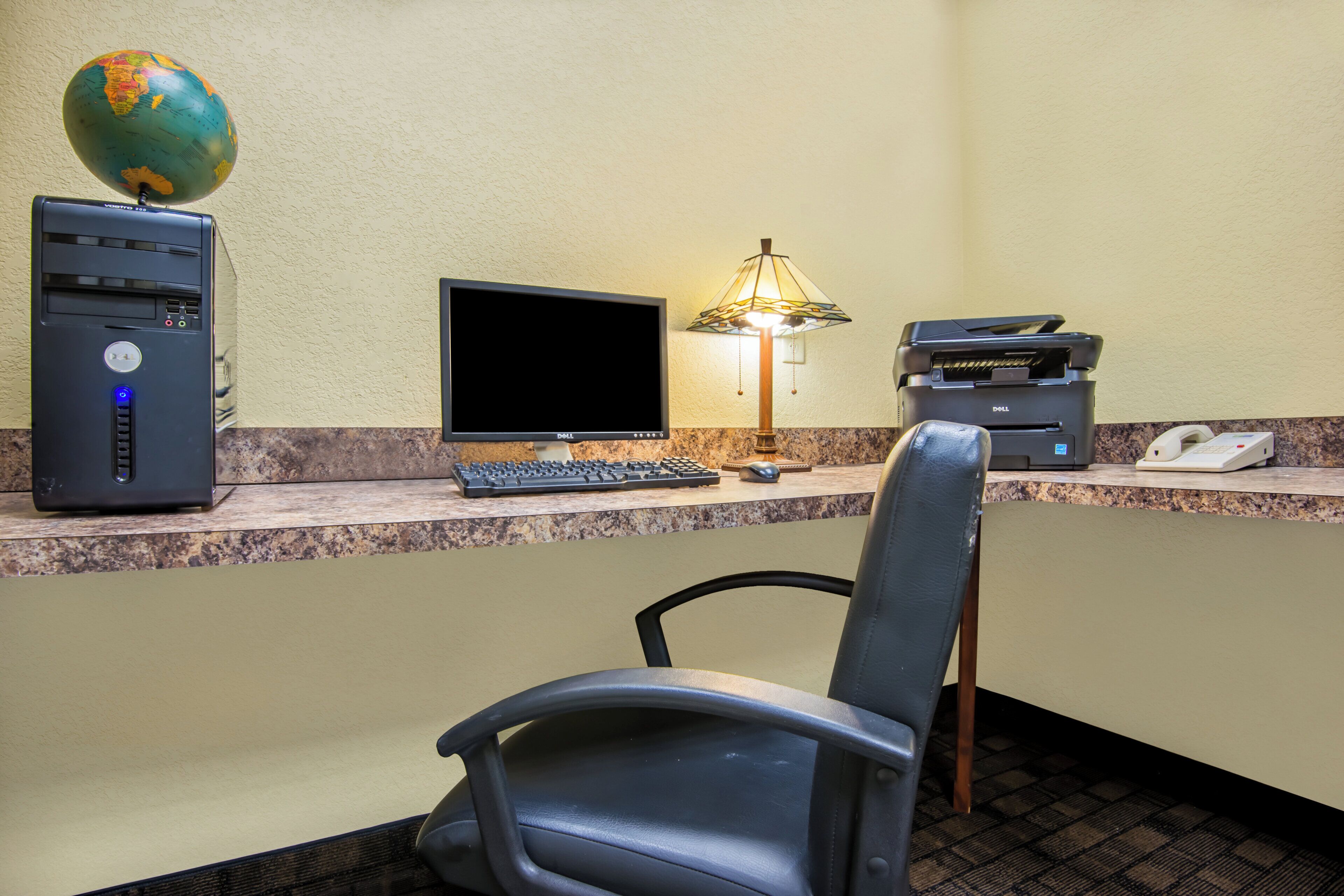 A hotel reception desk with a desktop computer, a flat-screen monitor, a lamp, a printer, and a telephone.