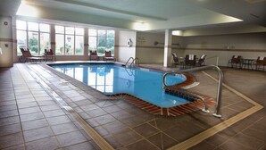 An indoor swimming pool with clear water, surrounded by lounge chairs and a tiled floor.
