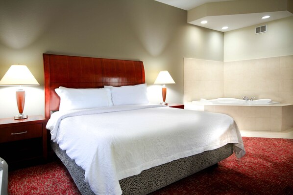 A hotel room with a large bed, two bedside tables with lamps, a red carpet, a bathroom with a bathtub, and a white wall.