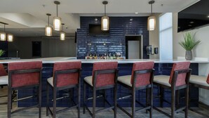 A modern bar area with dark blue tiled backsplash, multiple hanging pendant lights, and bar stools with red cushioned seats.