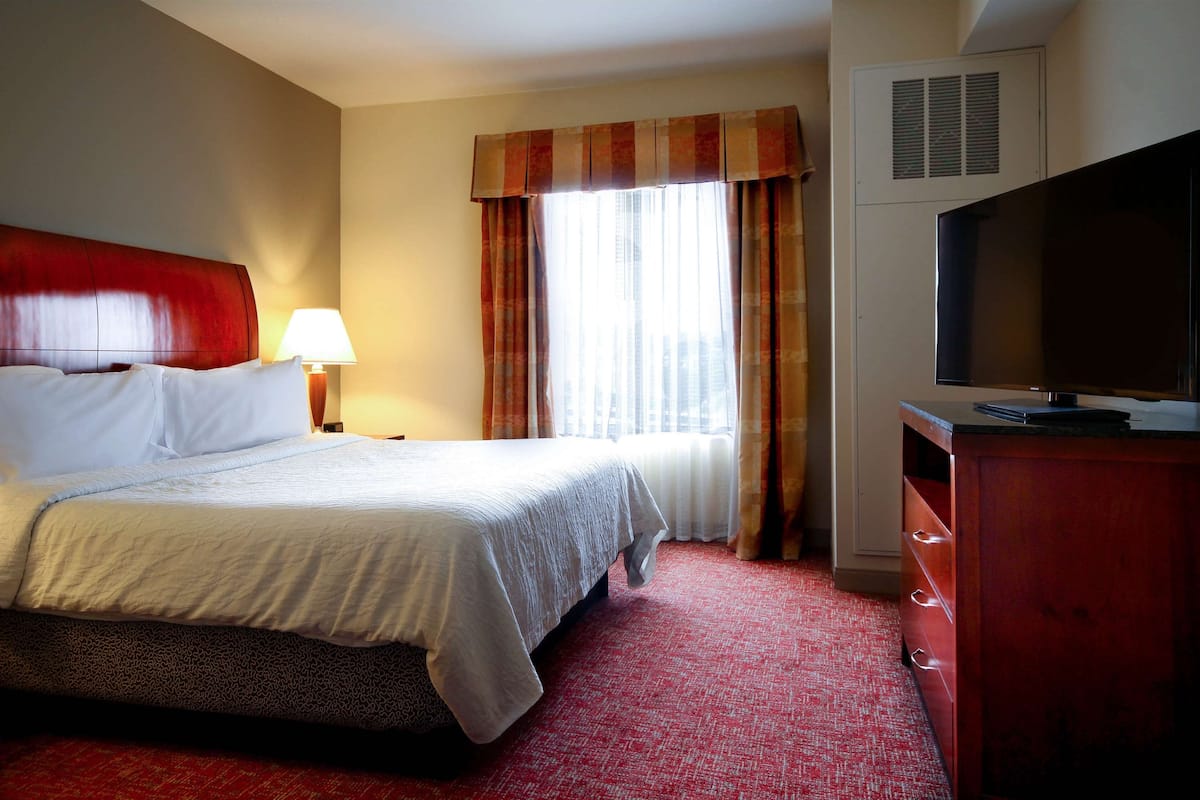 Ein Hotelzimmer mit Bett, Fernseher, Lampe und einem fenster mit Vorhängen.