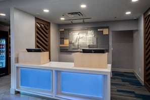 Een receptiebalie van een hotel met een modern design, inclusief een ontvangstruimte, een wandbord en een toonbank met een laptop.