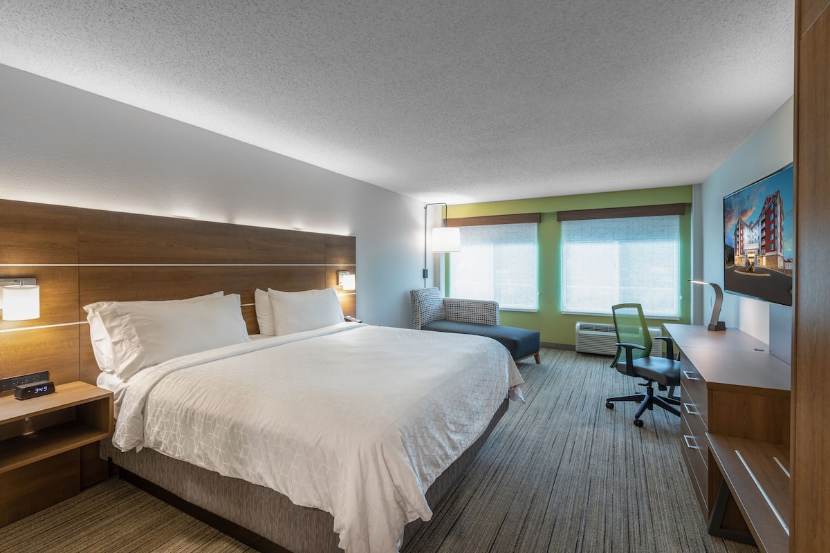 Une chambre d’hôtel avec un grand lit, un bureau, une chaise et une fenêtre donnant sur un beau paysage.