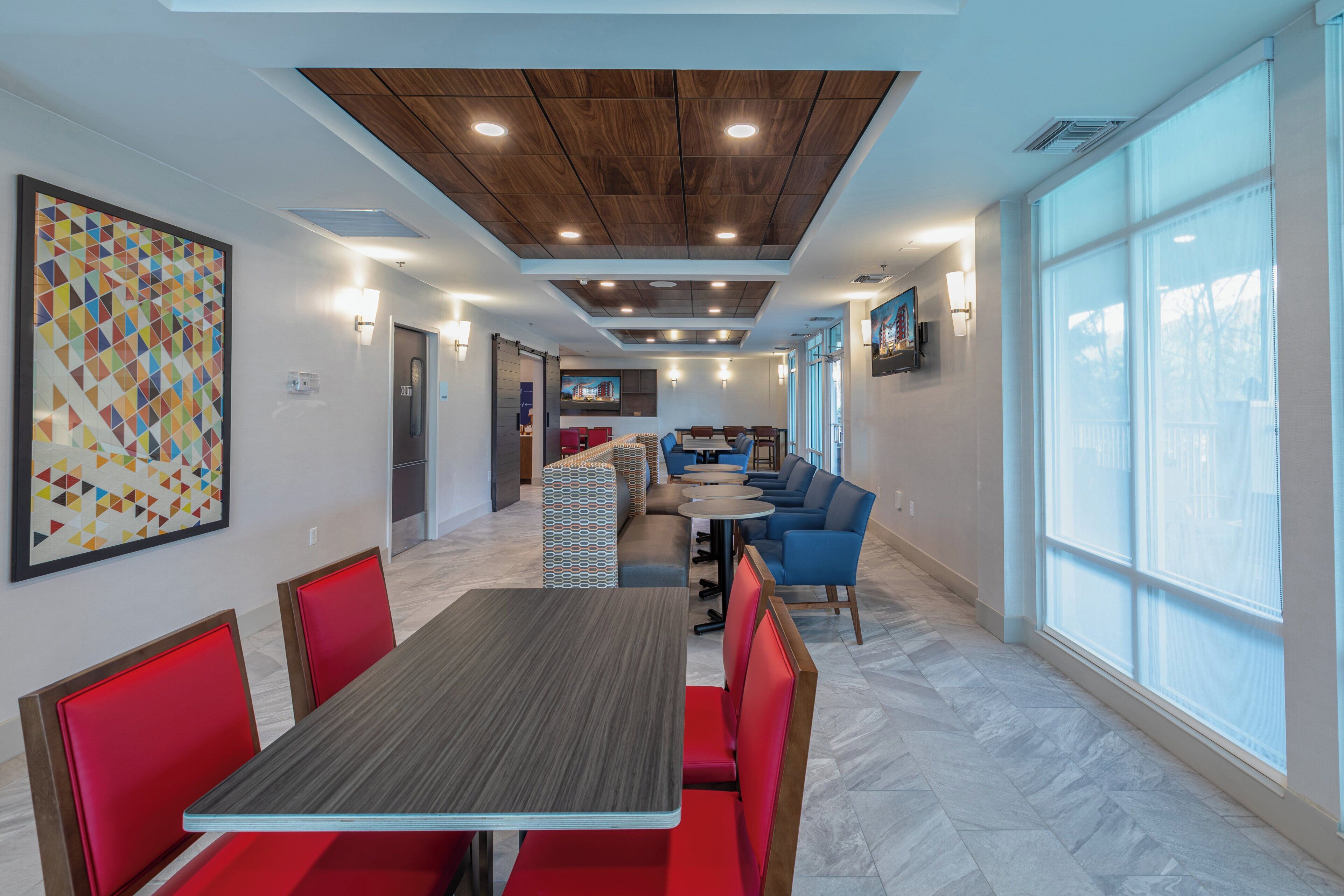 A modern dining area with a long table, red chairs, and blue sofas.