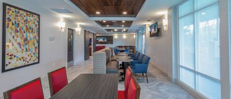 A modern dining area with a long table, red chairs, and blue sofas.