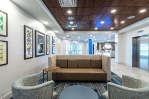 Eine moderne Lobby mit einer Couch, Sesseln, gerahmten Kunstwerken und einem Empfangstresen.