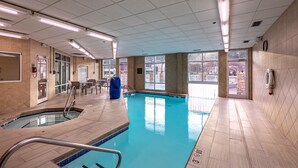 Een binnenzwembad met helder water, betegelde wanden en een plafond met fluorescentie verlichting.