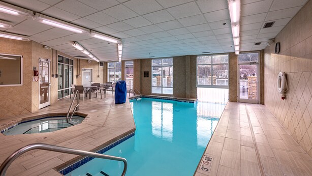 Een binnenzwembad met helder water, betegelde wanden en een plafond met fluorescentie verlichting.
