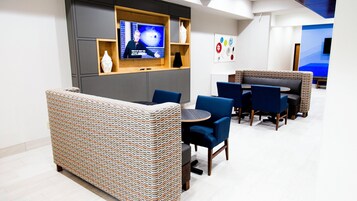 Un espacio lounge moderno con televisor, asientos y decoración mural.