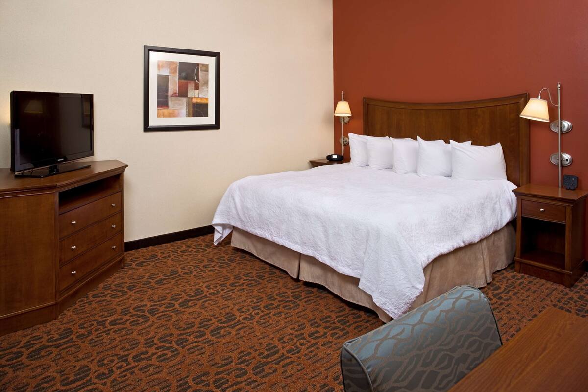 Une chambre d’hôtel avec un grand lit, un téléviseur posé sur une commode en bois et une moquette à motifs.