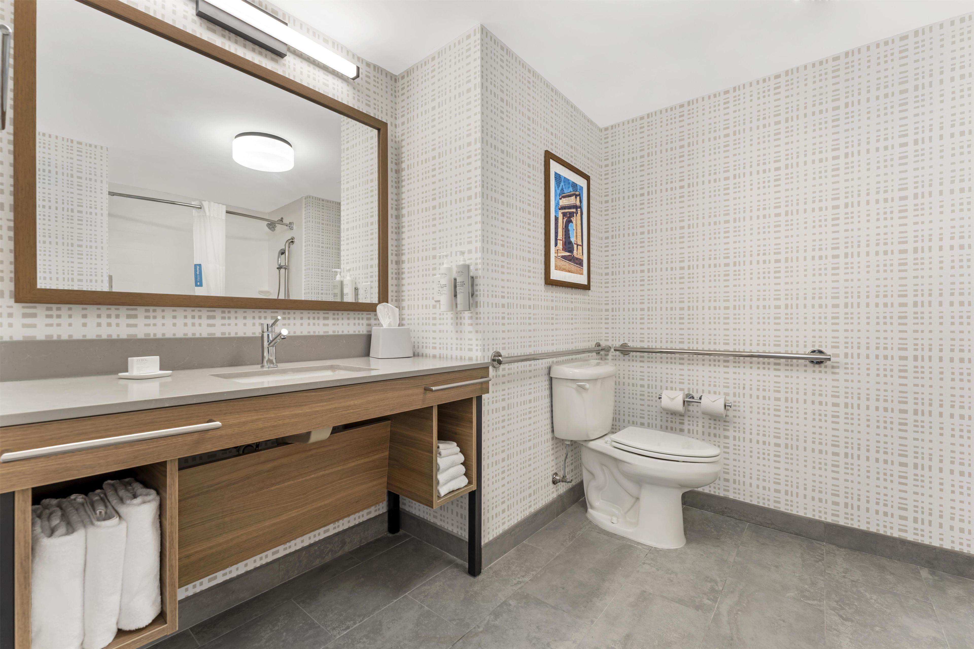 A modern bathroom with a large mirror, a sink with a towel rack, a toilet, and a shower area.