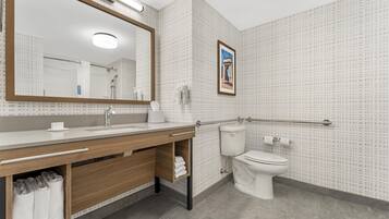 A modern bathroom with a large mirror, a sink with a towel rack, a toilet, and a shower area.