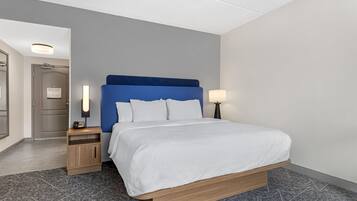 A hotel room with a bed, bedside tables, a nightstand, a lamp, and a door.