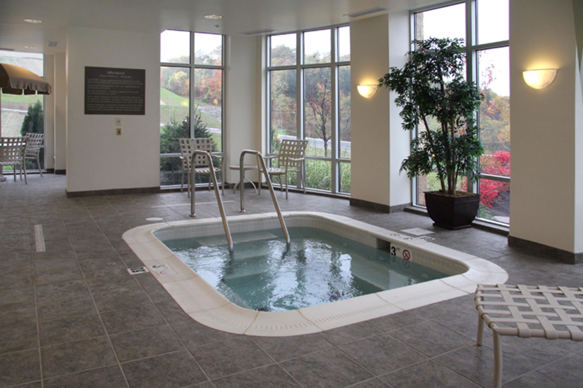 A hot tub with a view of a park through large windows.