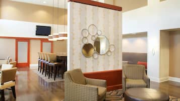 A hotel lobby with a seating area, a television mounted on the wall, and a decorative wall panel.