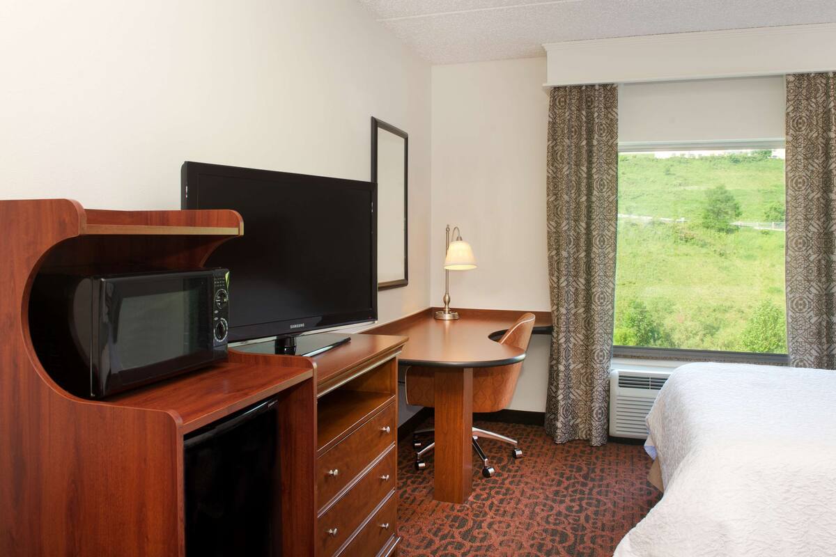 Une chambre d’hôtel avec un lit, un bureau avec une télévision, un four à micro-ondes et une fenêtre avec des rideaux.