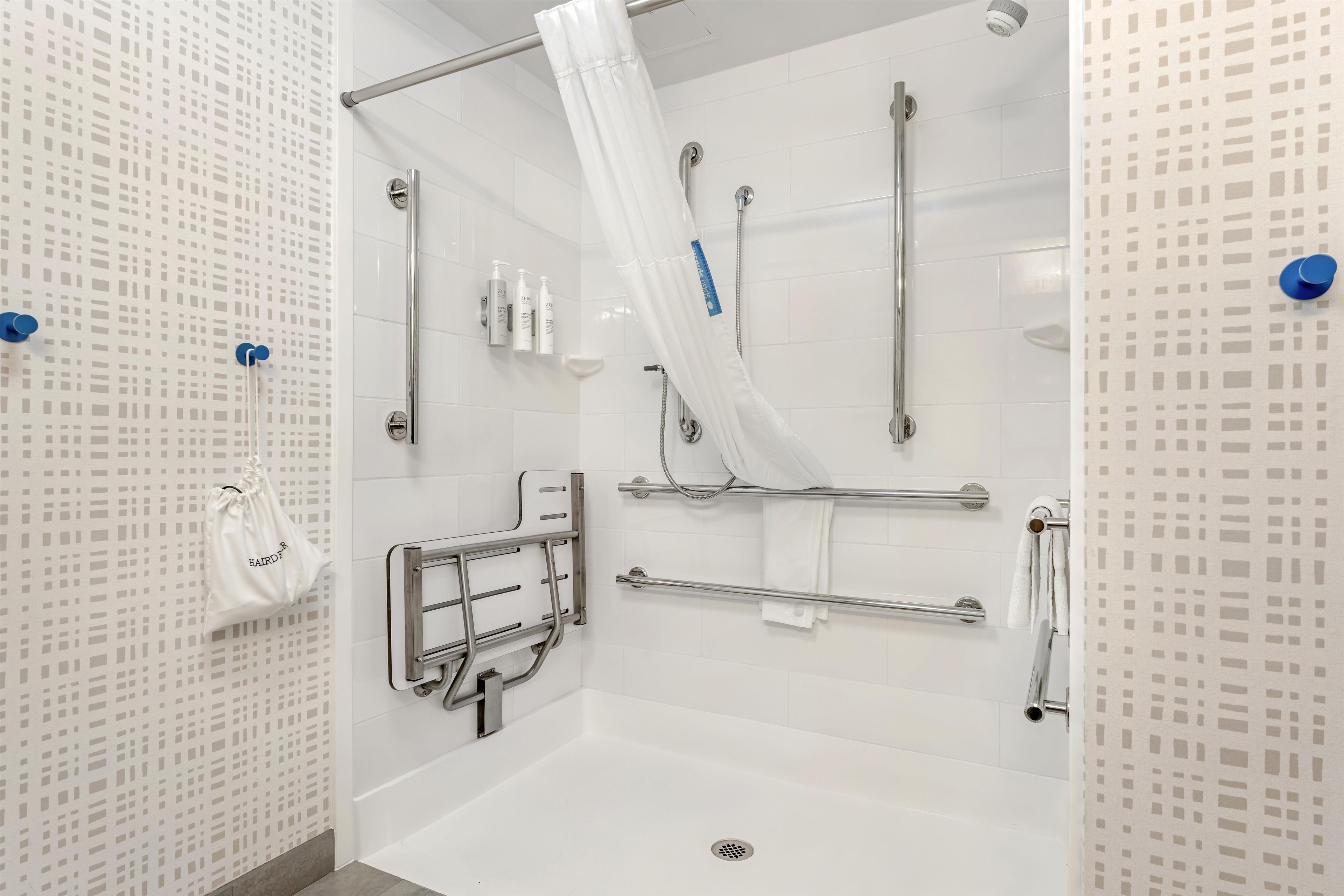 A modern bathroom with a walk-in shower, grab bars, and a white tiled wall.