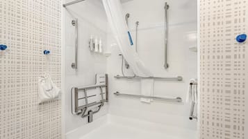 A modern bathroom with a walk-in shower, grab bars, and a white tiled wall.